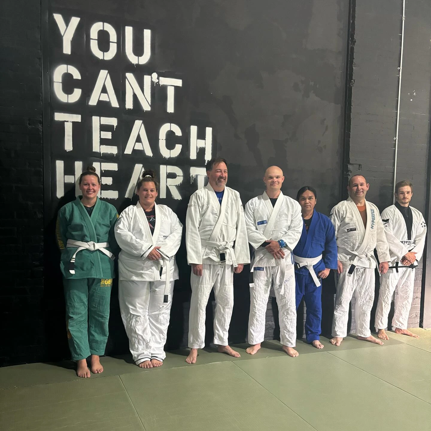 white belt adults lined against a wall with a mural that says you can't teach heart